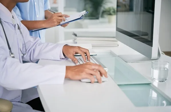 Profissionais de saúde trabalhando no computador e preenchendo uma ficha.