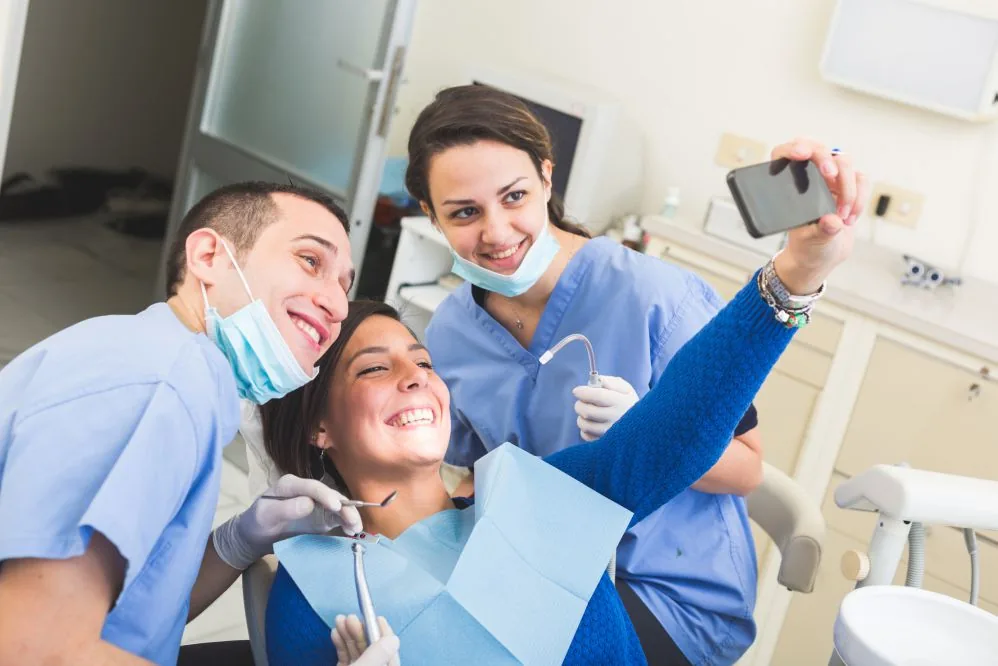 Paciente e profissionais de odontologia tirando uma selfie no consultório.
