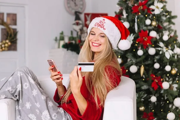 Mulher usando o celular junto a uma árvore de Natal.