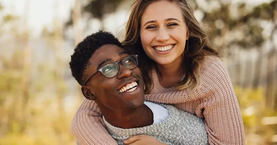 Casal sorrindo e se abraçando ao ar livre.
