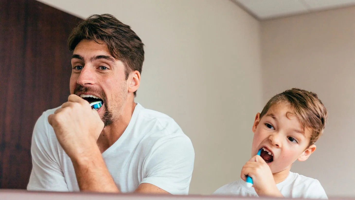 Pai e filho escovando os dentes juntos.