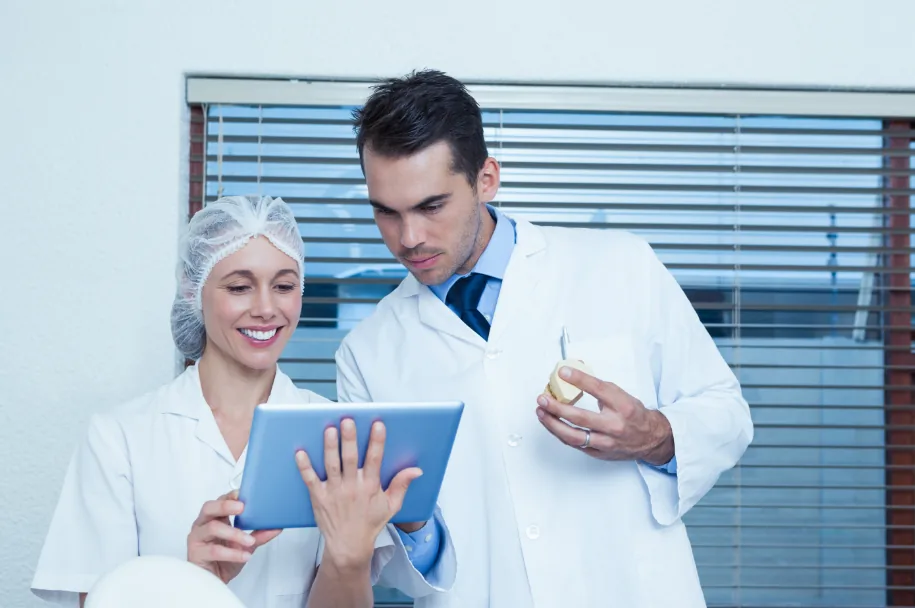 Dentistas consultando um tablet e um modelo de arcada dentária.