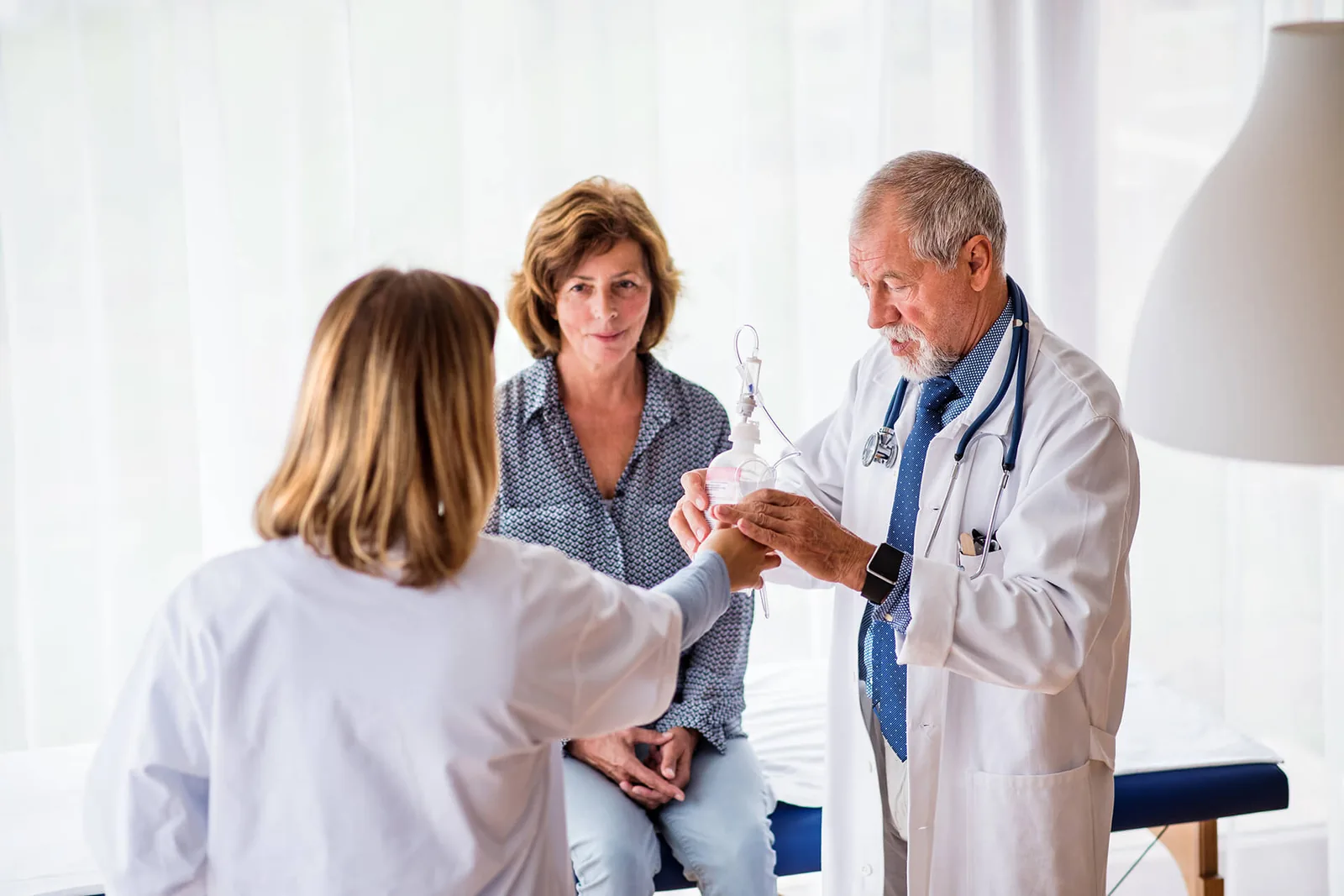 Médico conversando com uma paciente e outra profissional no consultório.