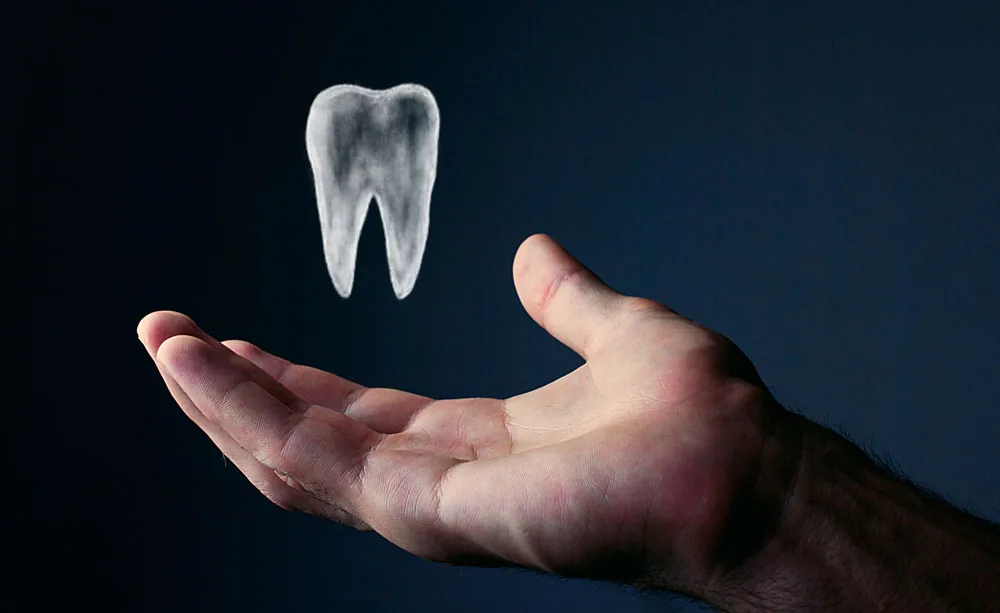 Ilustração de um dente acima de uma mão aberta.