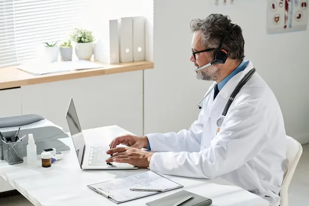 Médico usando computador com um fone de ouvido e microfone.
