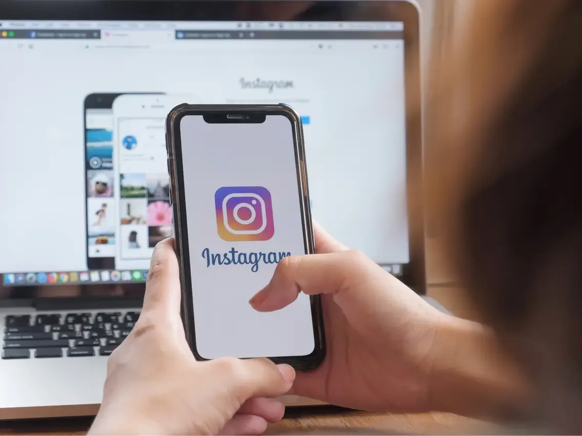 Pessoa abrindo o Instagram no celular diante de um computador.