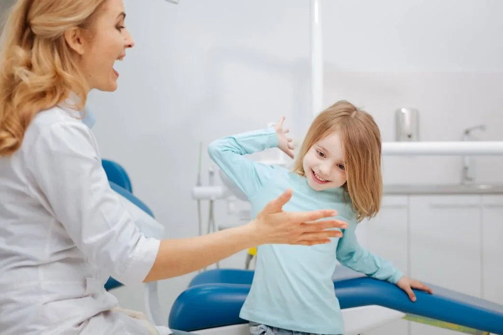 Dentista conversando com uma criança e sua responsável no consultório.